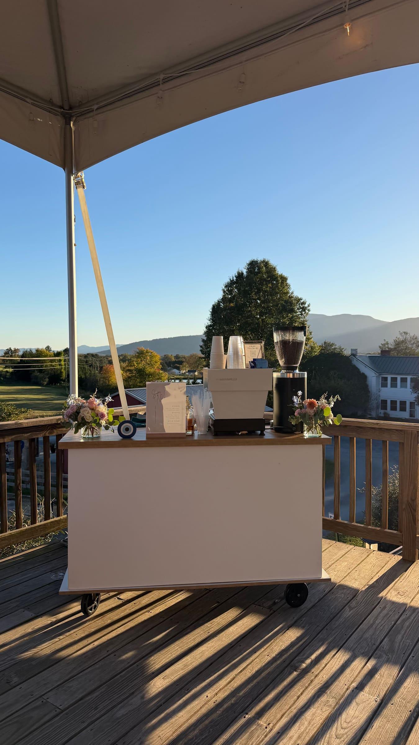 The Atelier cart under a tent on a wooden deck at sunset, with mountains on the horizon