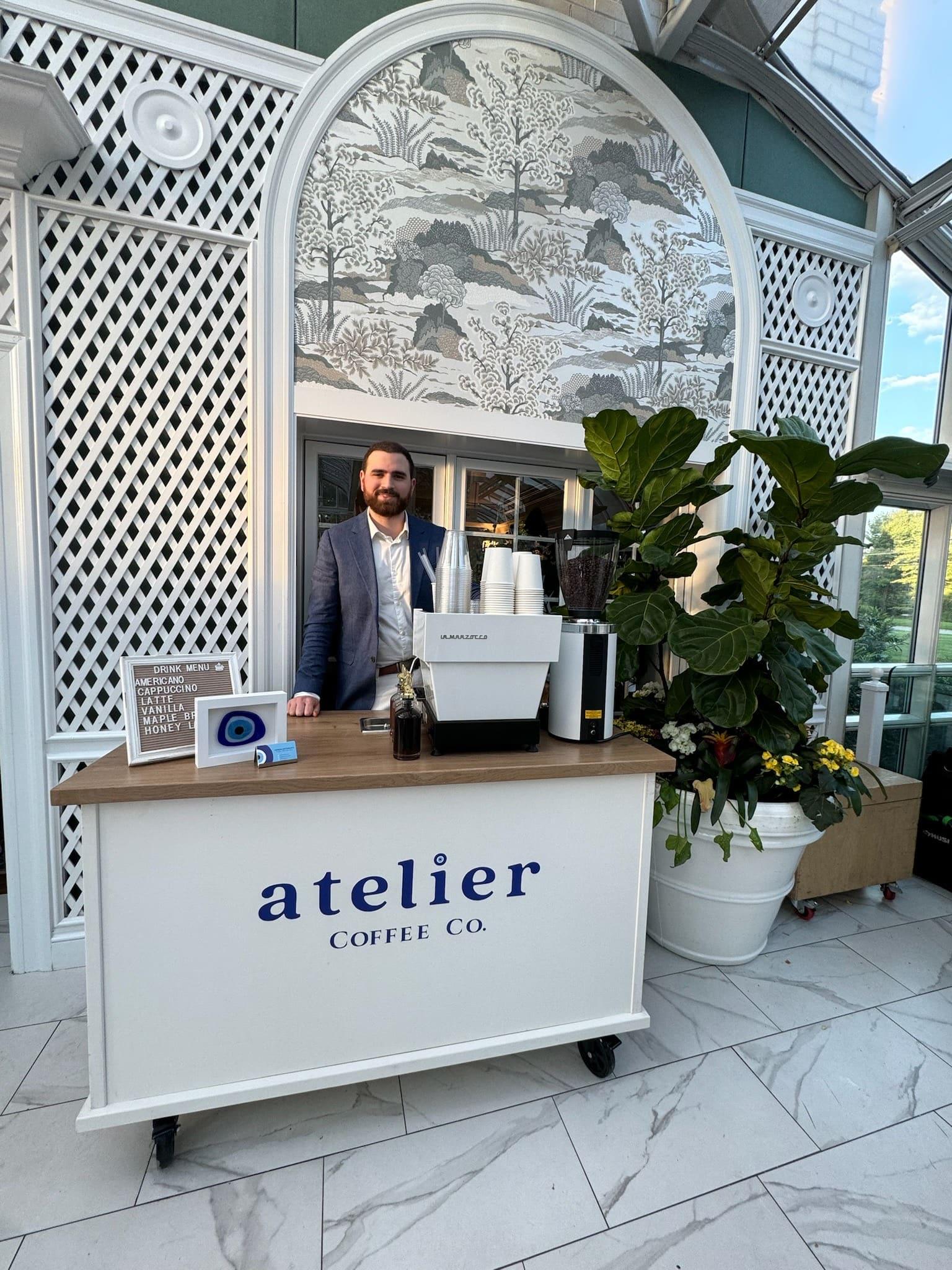The Atelier Coffee Co. cart in a glass conservatory with white lattice walls and potted plants, a barista behind it