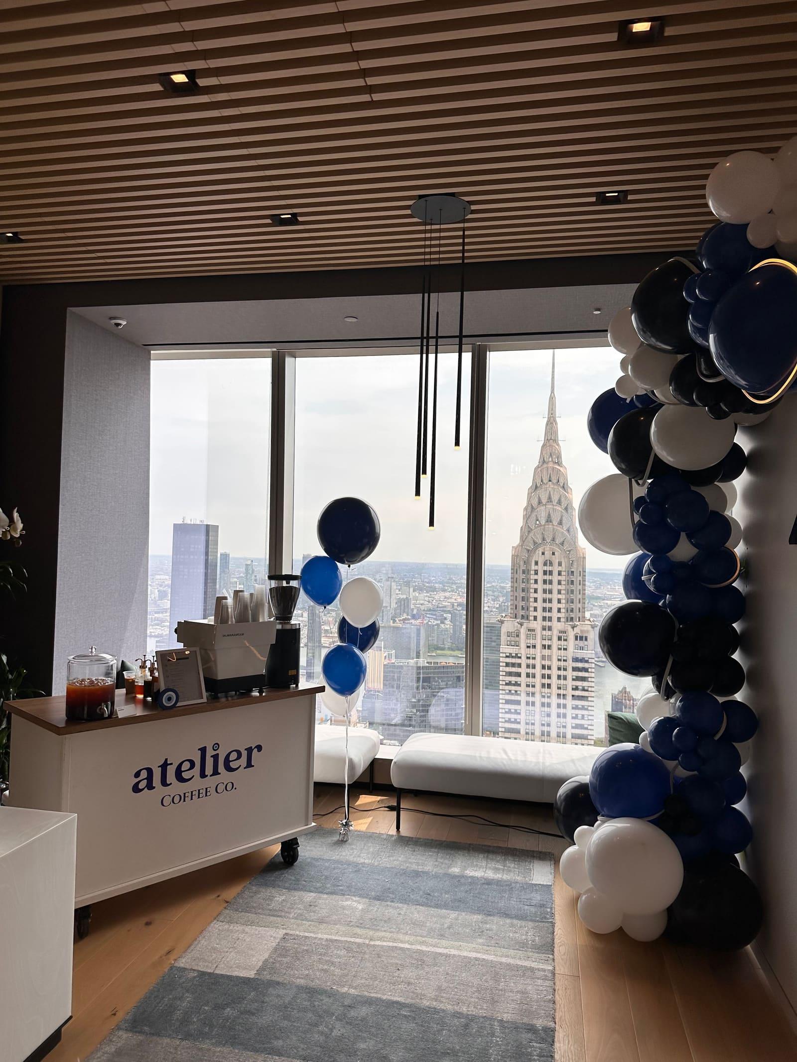 The Atelier cart in an office lounge with blue and white balloons and the Chrysler Building in the window