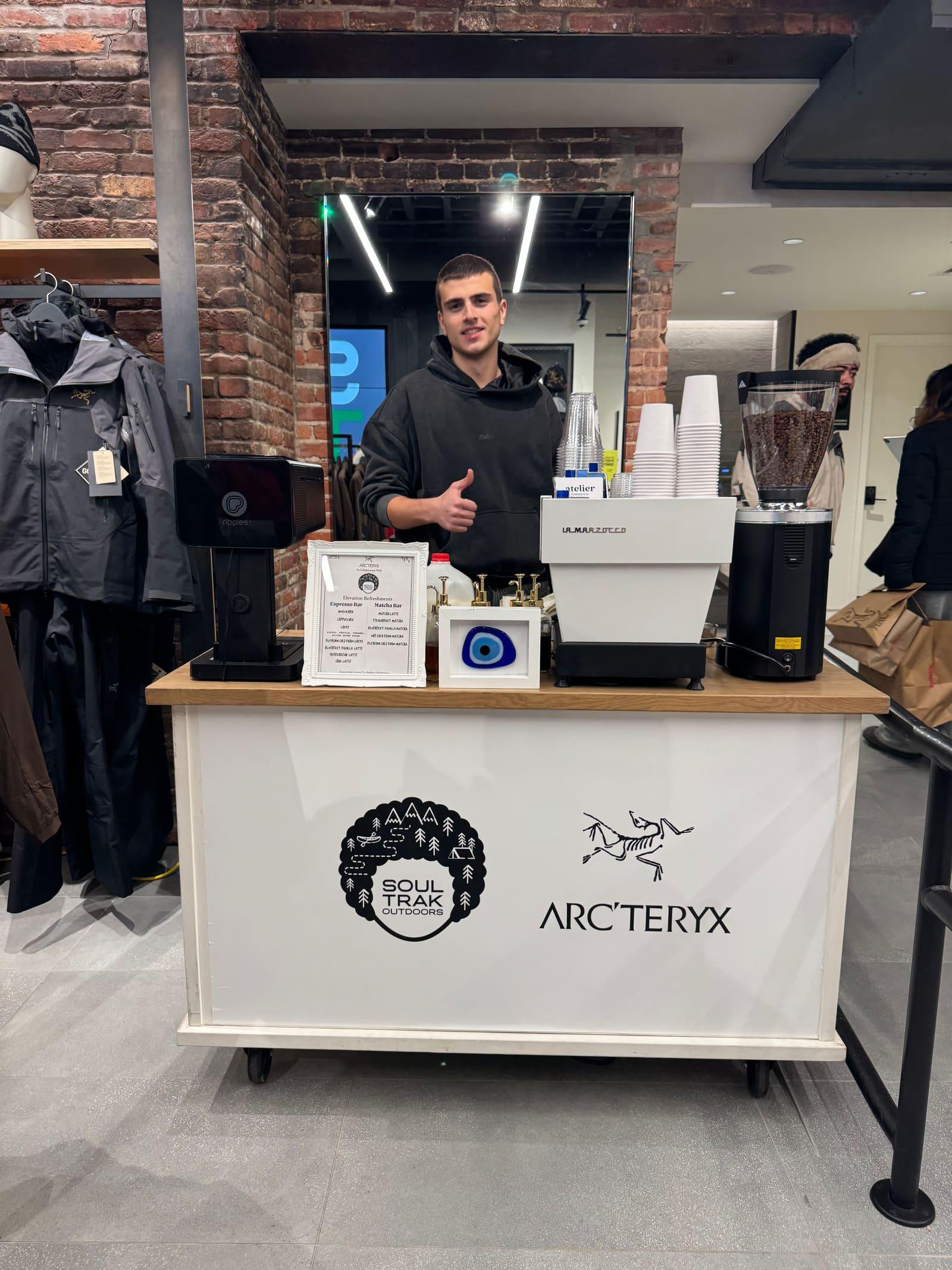 An Atelier barista gives a thumbs up behind an Arc’teryx branded espresso cart on the shop floor