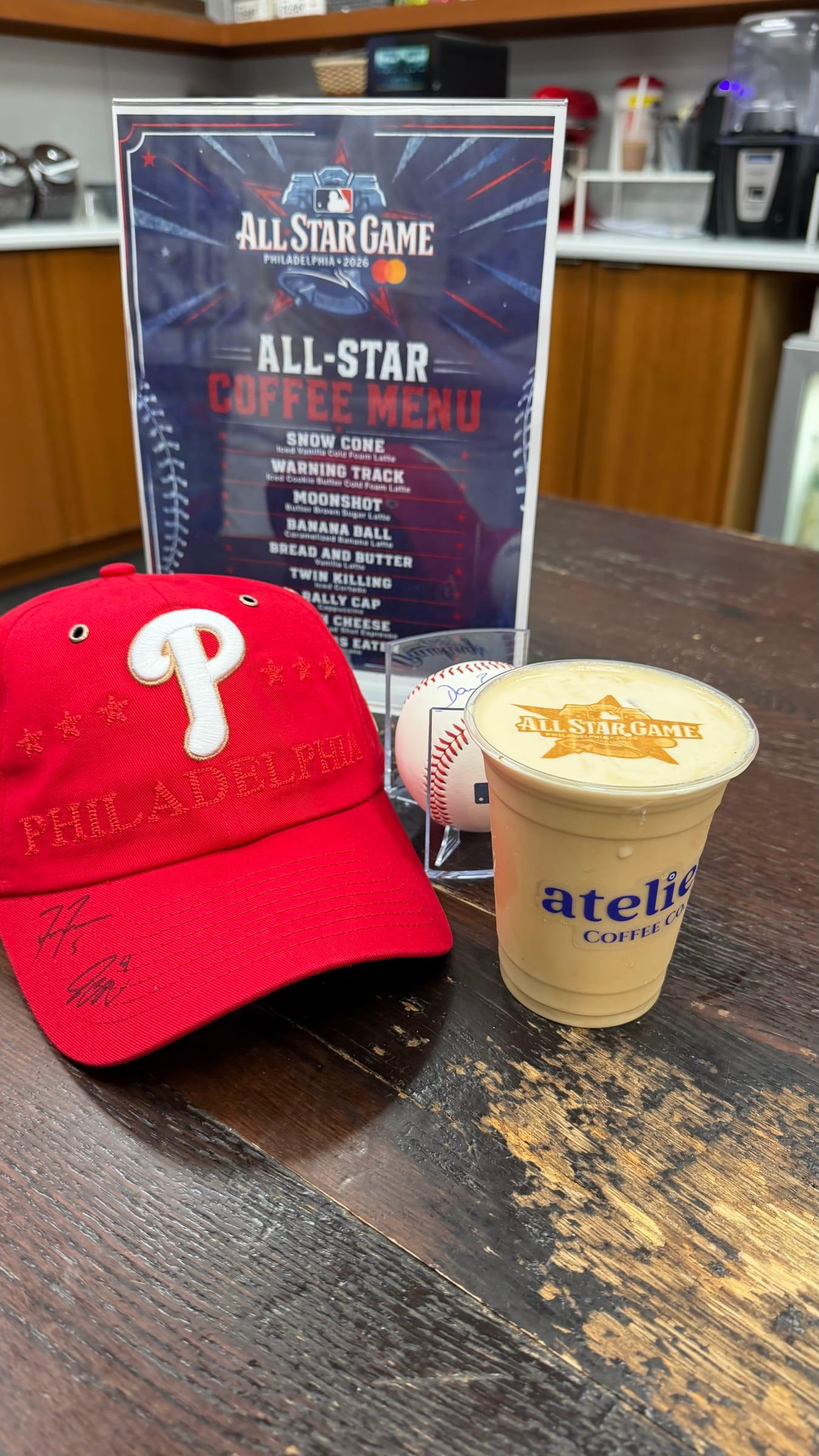 A themed coffee menu beside a signed Phillies cap and a latte with the event logo printed on the foam