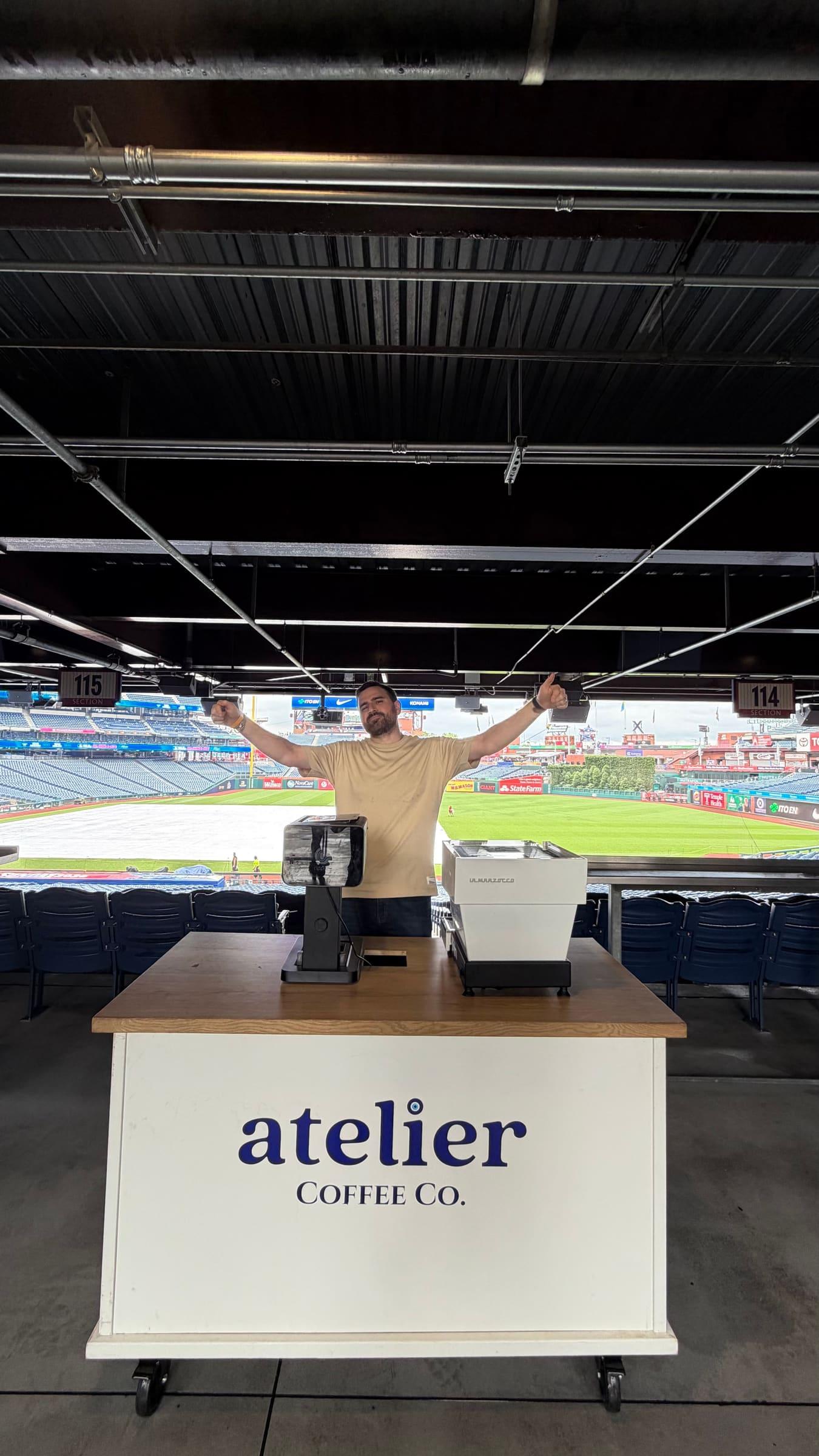 An Atelier barista with arms raised behind the cart, in a suite that opens onto the ballpark