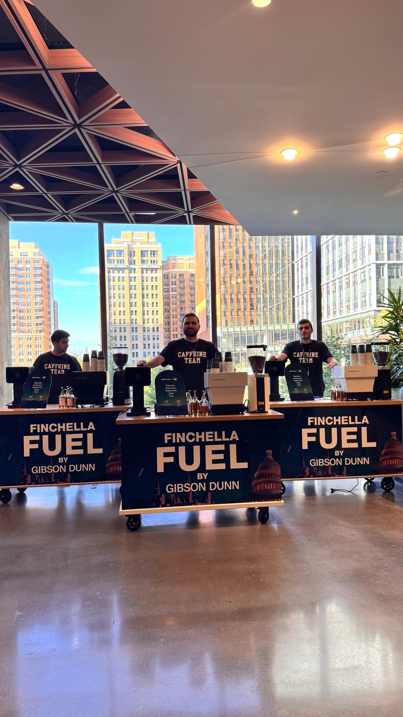 Three espresso carts wrapped in a sponsor’s branding, staffed by Atelier baristas in a sunlit conference space