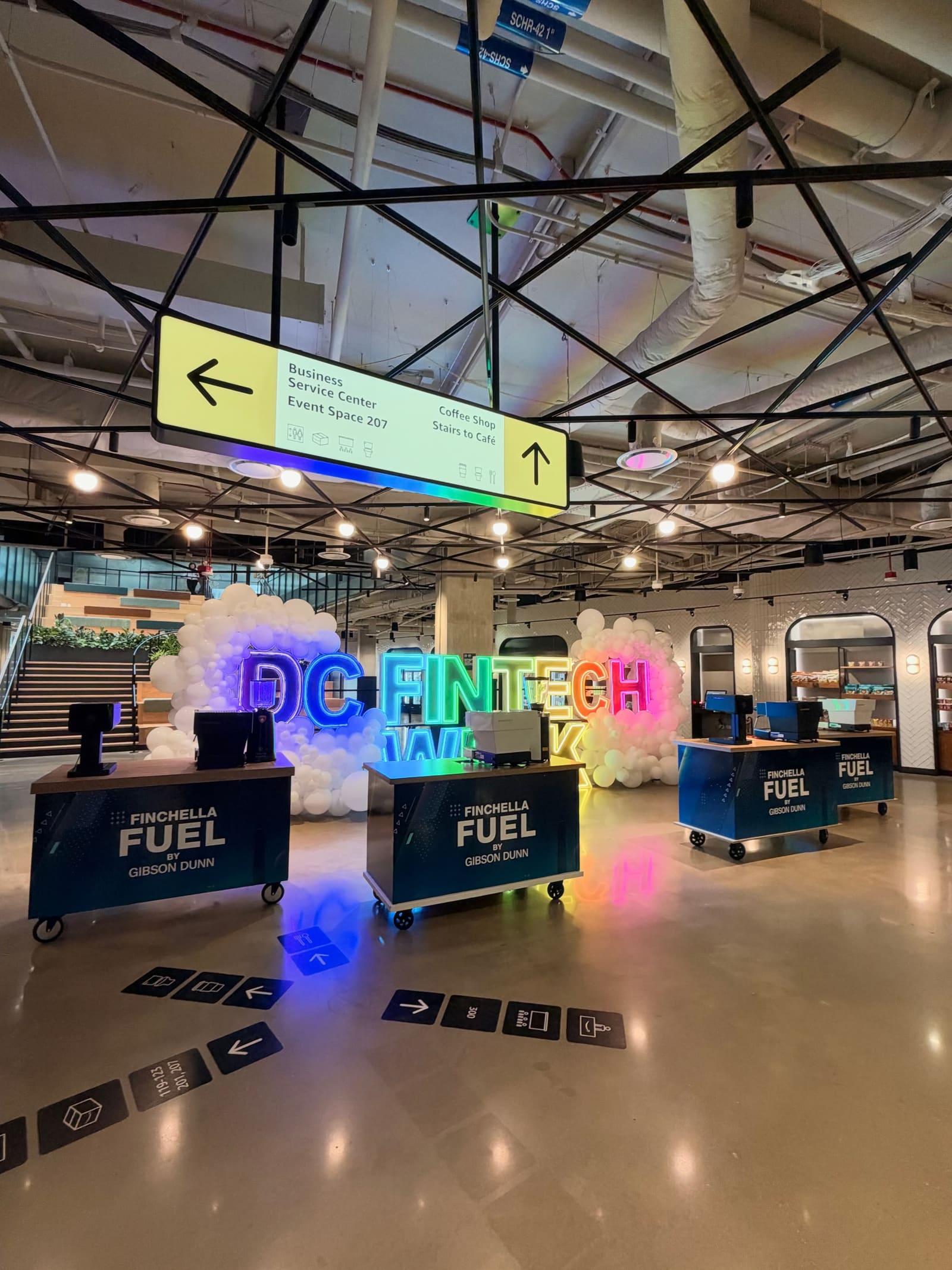 Three branded espresso carts on a conference hall floor, in front of a glowing neon DC Fintech Week sign