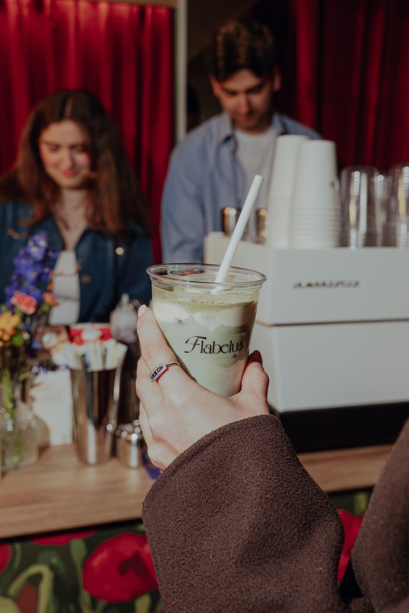 A guest holds an iced matcha in a branded cup while baristas work the cart behind