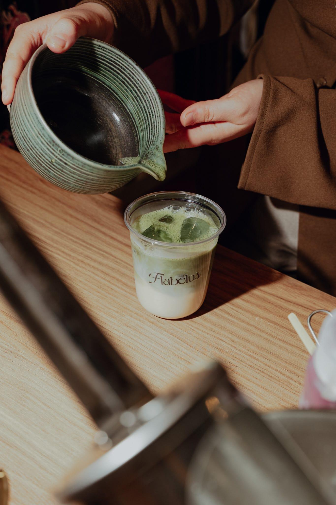 Matcha poured from a ceramic pitcher into a branded cup