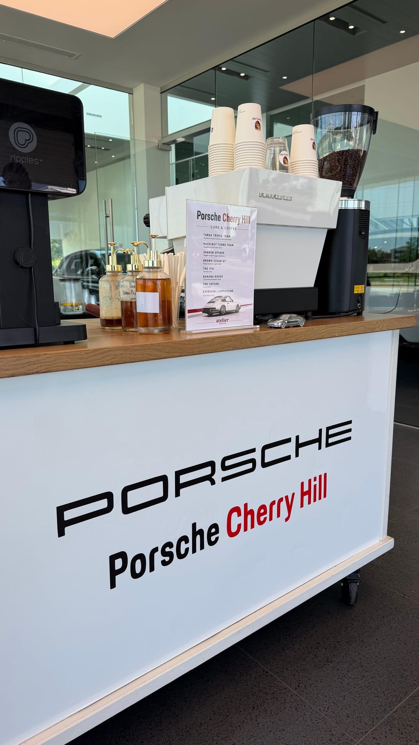 A Porsche Cherry Hill branded espresso cart set up with a drinks menu, house syrups and a grinder
