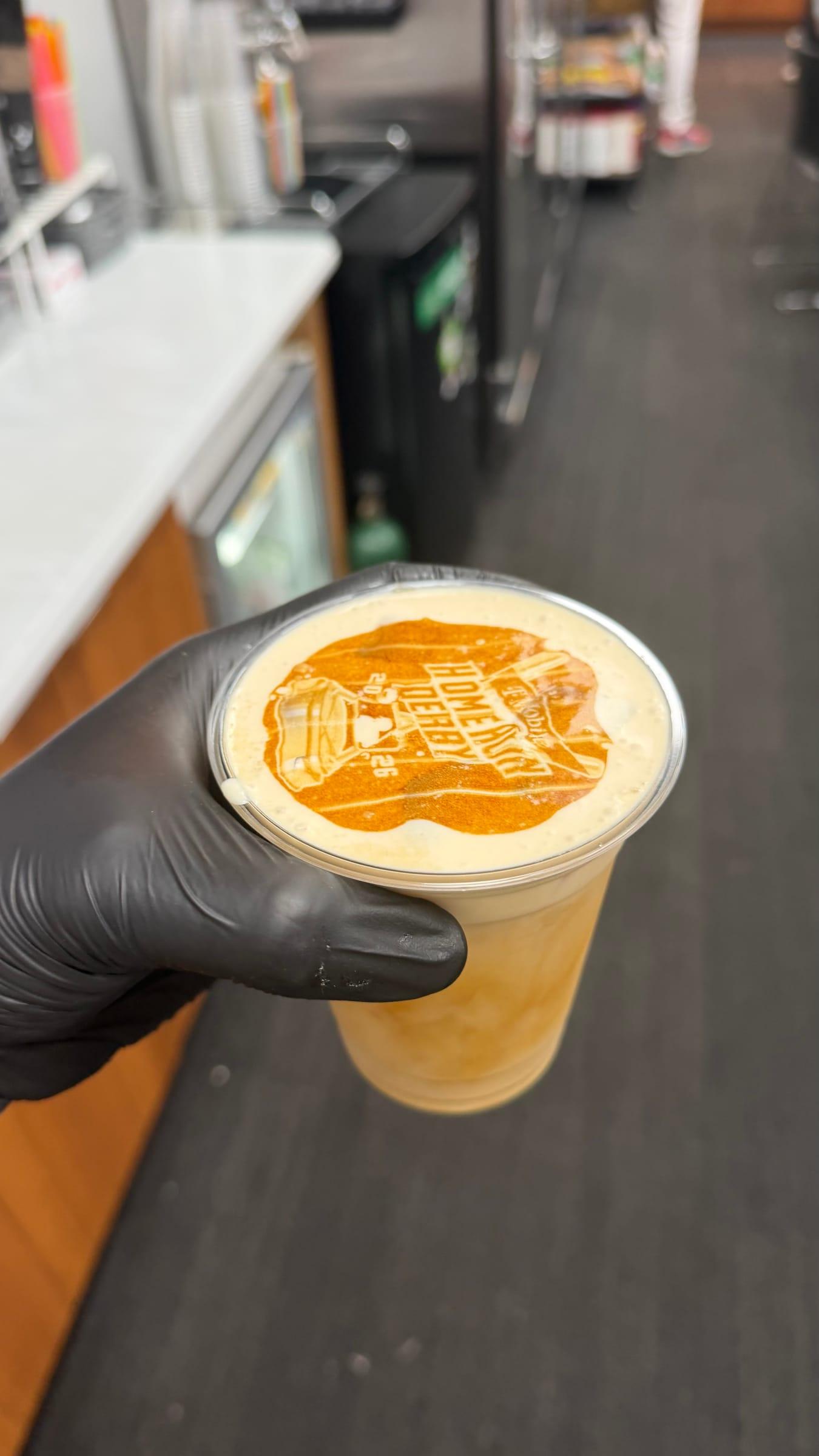 A gloved hand holding an iced latte with an event logo printed on the foam